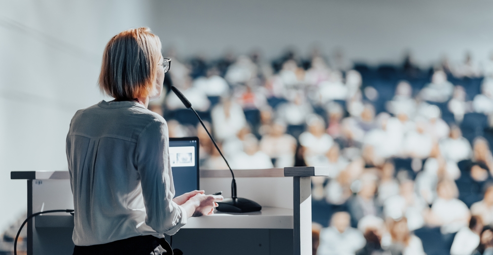 A blonde-haired woman talks to a room of people at a research seminar